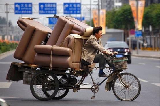 Pekin’de bir adam koltuklarla istiflenmiş üç tekerlekli bir bisiklet kullanırken.